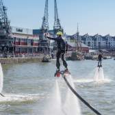 A man wearing a water-powered jetpack performing stunts on Bristol's Harbourside during the Bristol Harbour Festival with the M Shed local history museum in the background - credit Jim Cossey