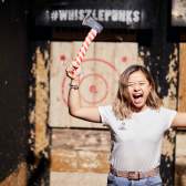 A woman cheering while holding two axes at the Whistle Punks Bristol Axe Throwing experience - credit Whistle Punks