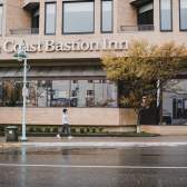 A person walks past The Coast Bastion Inn on a rainy day, with wet pavement and trees lining the street.
