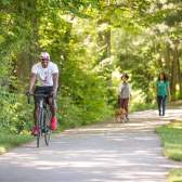 Man riding bike and women walking along wooded rail trail
