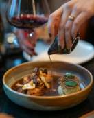 Hand Pouring Sauce Over a Plated Entr e with a Glass of Red Wine Nearby