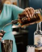 Person pouring bourbon into a measuring shot glass