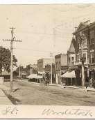 sepia toned photo of historic Main Street in 1909 featuring brick buildings and a dirt road