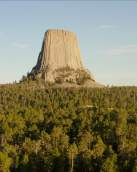 Aerial view of Devils tower above treeline and a blue sky