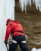 Aaron Mulkey in a red jacket and helmet standing next to a large icicles