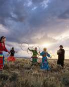 Women holding hoops hoop dancing and man playing drum under cloudy sky