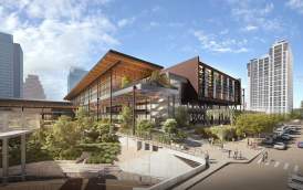 Austin Convention Center rendering shows the new building from street level, looking towards the East Entrance. Pedestrians cross the street, with Hilton Austin Hotel in the background and Waller Creek  with trees, native plants and a creek-side walkway in the foreground.