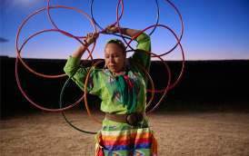 Woman holding hoops in a rodeo arena at sunset dressed in regalia