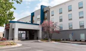 Exterior of Hampton Inn and Suites Leesburg Virginia, a modern four-story hotel with teal and gray facade, covered porte-cochere entrance and landscaped parking area