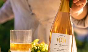 Bottle of Oh's Vineyard 2023 sparkling rosé brut nature held at an outdoor table with a filled glass in Loudoun