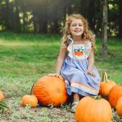A young girl smiles at a pumpkin patch with multiple pumpkins.