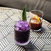 two cocktails, one purple, one brown, on a table