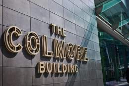 Raised golden signage lettering reads THE COLMORE BUILDING next to the building entrance under a glass canopy