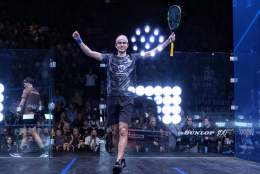 Squash player standing in play area holding arms and  racquet in the air in victory