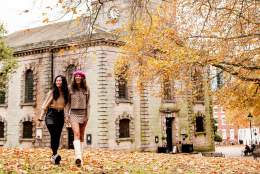 Two friends walking through a park in autumn with fallen orange and red leaves with St Phillip's Cathedral in the background