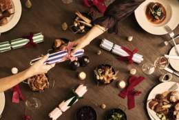 Festive dinner table with hands pulling a Christmas cracker. Plates of food, candles, and colourful wrapped crackers create a warm, celebratory atmosphere.
