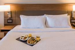 A neatly made bed with white linens, featuring a breakfast tray with two plates of food and two glasses of juice, exudes a cosy and inviting ambience.