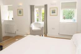 One of the bedrooms at The Plovery at Church Farm Cottages in East Yorkshire. The double bed has fresh white bed linen, three windows are flooding the room with light and a grey chair sits next to one of the windows.