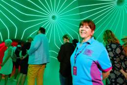 A hey volunteer at an event, with people in the background along with a bright green neon wall.