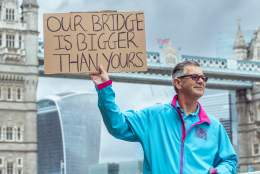 A HEY Volunteer in his iconic blue uniform stood in front of Tower Bridge in London holding a sign which says our bridge is better than yours, referring to the Humber Bridge in East Yorkshire.