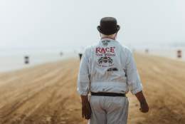 A man wearing Race the Waves overalls walking along the beach