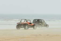 2 cars racing a long the beach with the sea in the background