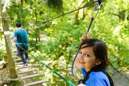 A girl and man walking across a rope bridge in the trees at Go Ape