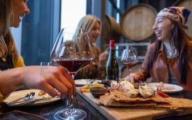 Friends_Sharing_Food_and_Red_Wine_at_a_Table_with_Wine_Barrels_in_the_Background