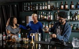 3 people standing behind the bar talking and making cocktails