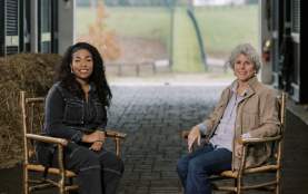 Two women in a barn in rocking chairs with rolling hills in the background