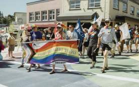 A group of people marching on the street with a pride flag.