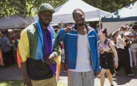 Two men smiling with a pride flag draped across ones shoulder.