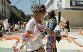 Person walking on the street handing out pride themed items. like flags, necklaces, and flowers.