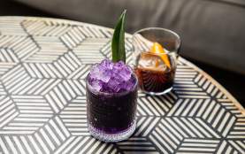 two cocktails, one purple, one brown, on a table