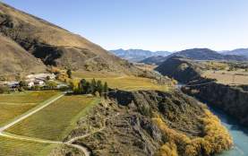 Overview of Gibbston in autumn with orange vineyards with mountains in the background and river flowing through the middle
