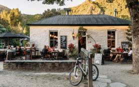 Old white cottage-looking pub with people sitting al fresco and green mountains in the background