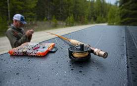 fly fishing line and tackle on a flat surface set in front of a fisherman tying a line