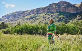 Woman standing in field against backdrop of rocky hillside dressed in regalia