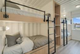 Wide shot of a bunk bedroom. The style is industrial chic, with black metal ladders and light wooden frames.