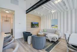 A cozy living room with two blue swivel chairs and a gray sectional. One wall is light brown shiplap and the other is the inside of a shipping container.