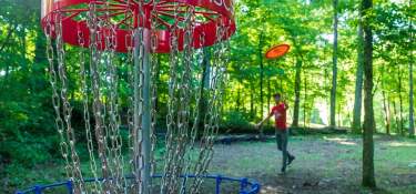 A man throwing a disc to a chain basket at Idlewild Disc Golf course