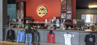 A man waiting for his order at the bar of Esoteric Brewing's taproom with a red wall bearing the Esoteric logo in the background