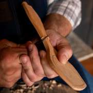 Person holding a utensil that they're carving out of wood.