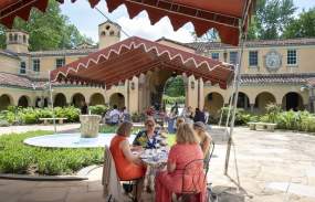 Groups of people dine outside Caramoor's buildings.