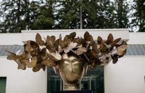 A bronze sculpture of a person's head adorned with a wreath of butterflies on display outside the Katonah Museum of Art.