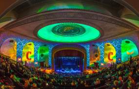 A crowd is gathered for a concert inside The Capitol Theatre. The room is awash in green and yellow lighting.