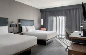 A hotel room with two beds that have white comforters. The curtains and carpet are grey.