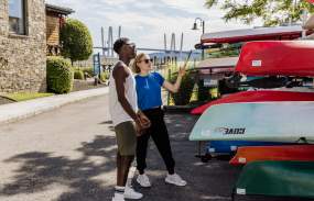 Two people stand next to a group of kayaking, getting ready to choose one and go out on the Hudson River.