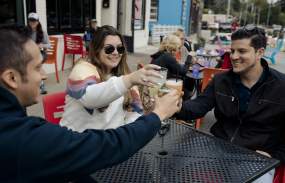 Three adults sit outside the Taco Dive Bar in Peekskill sharing a toast.