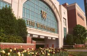 The outside of the building with light stone and glass plus a sign that says "The Westchester."